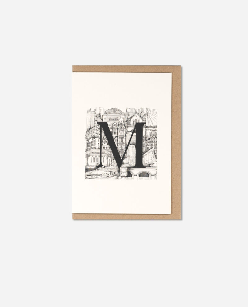 Flat lay of M for Manchester greeting card showing black letter M over detailed Manchester cityscape illustration on cream card