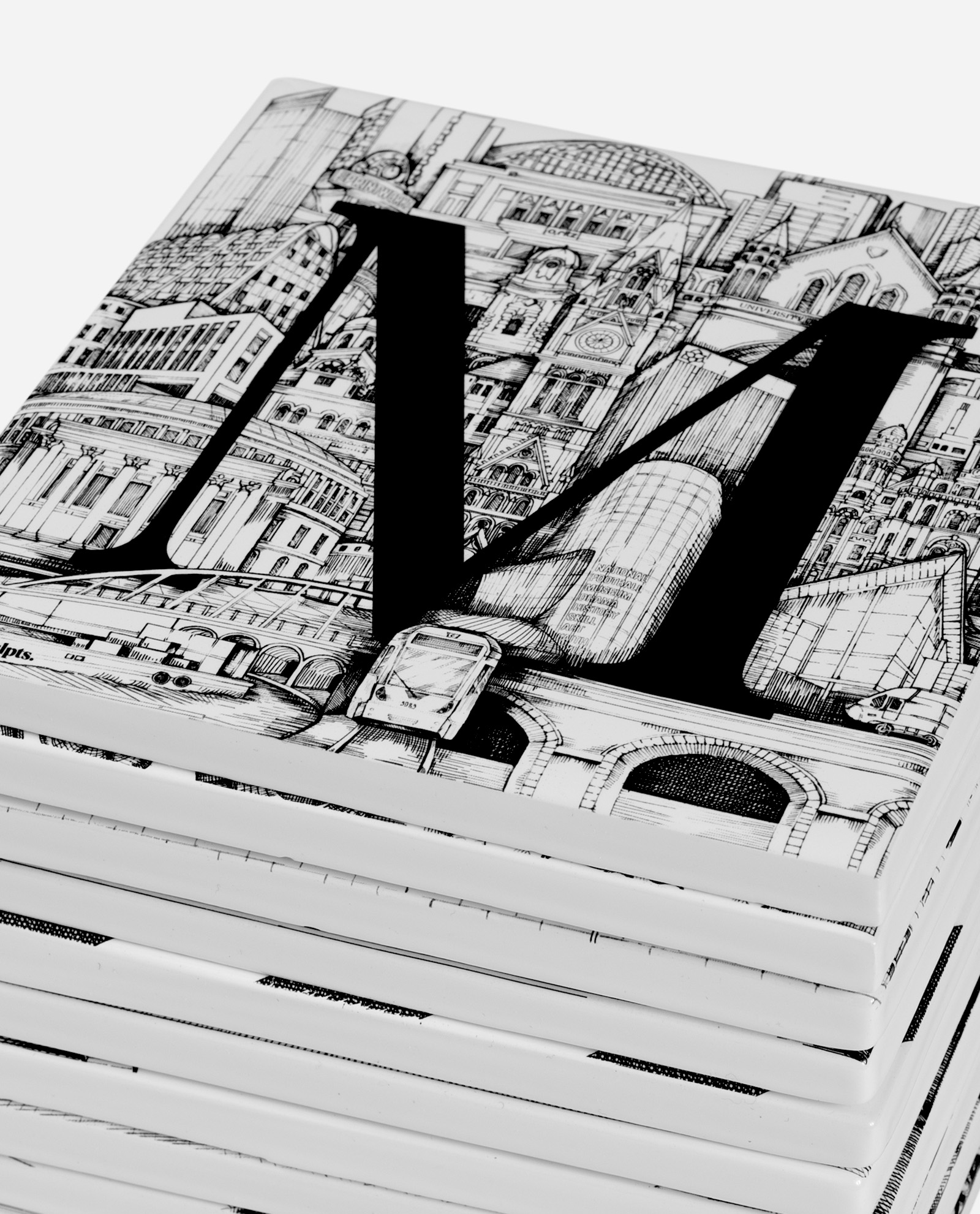 Close-up angled view of Manchester Tile Set showing detailed black letter M and architectural illustrations on white ceramic tiles